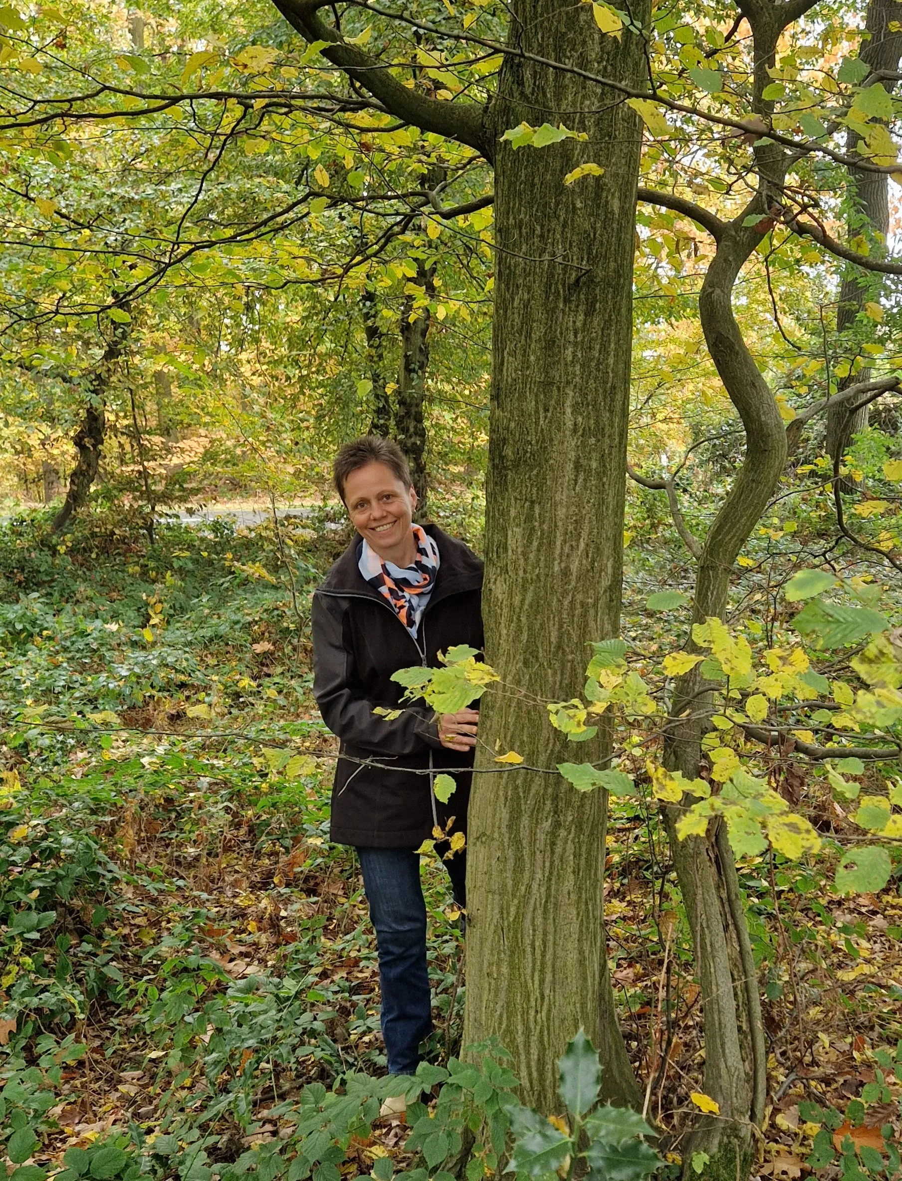 Astrid lehnt an einem Baum im herbstlichen Wald