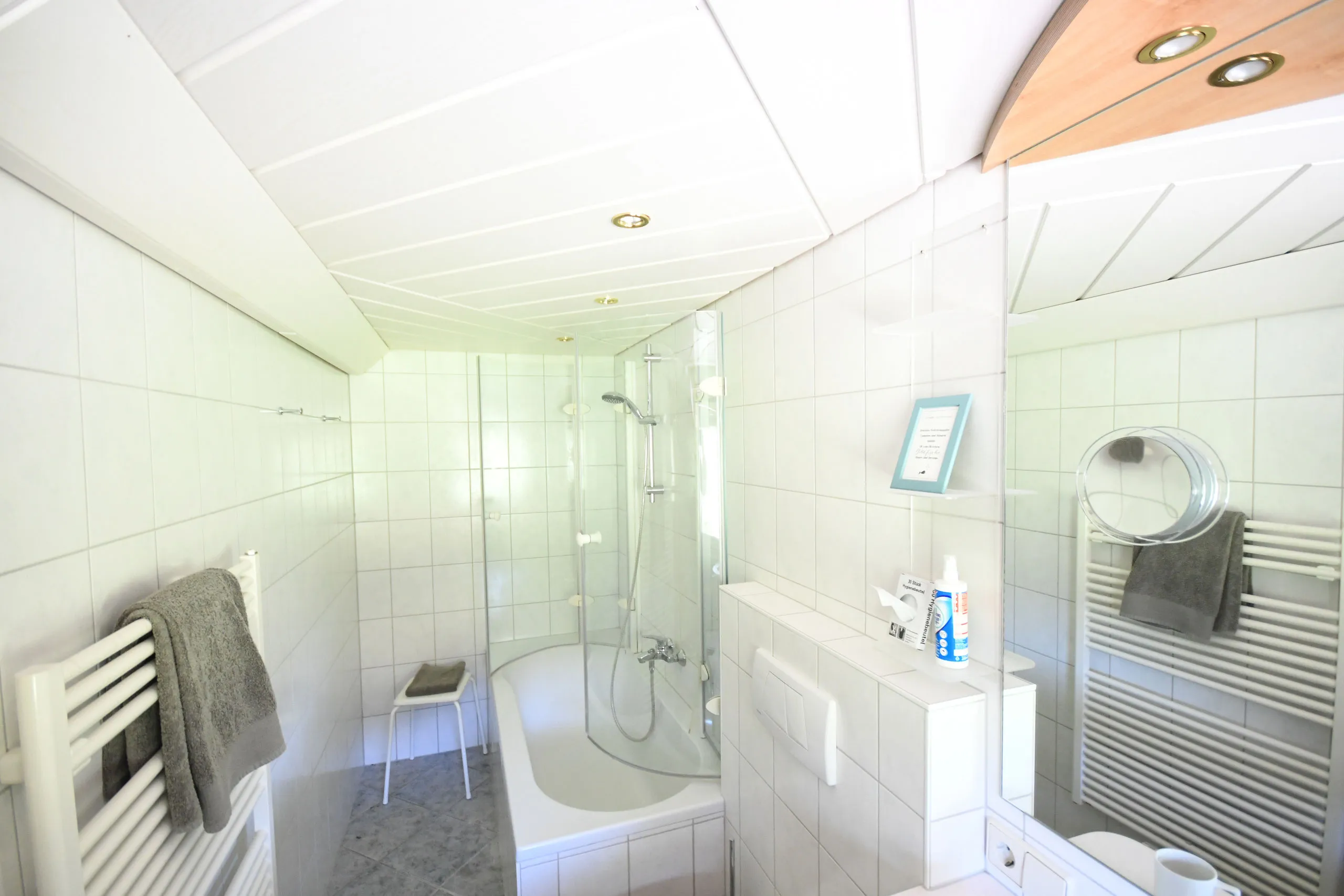 Ein weiß gefliestes Bad mit Dusche, Badewanne und Handtuchheizkörper