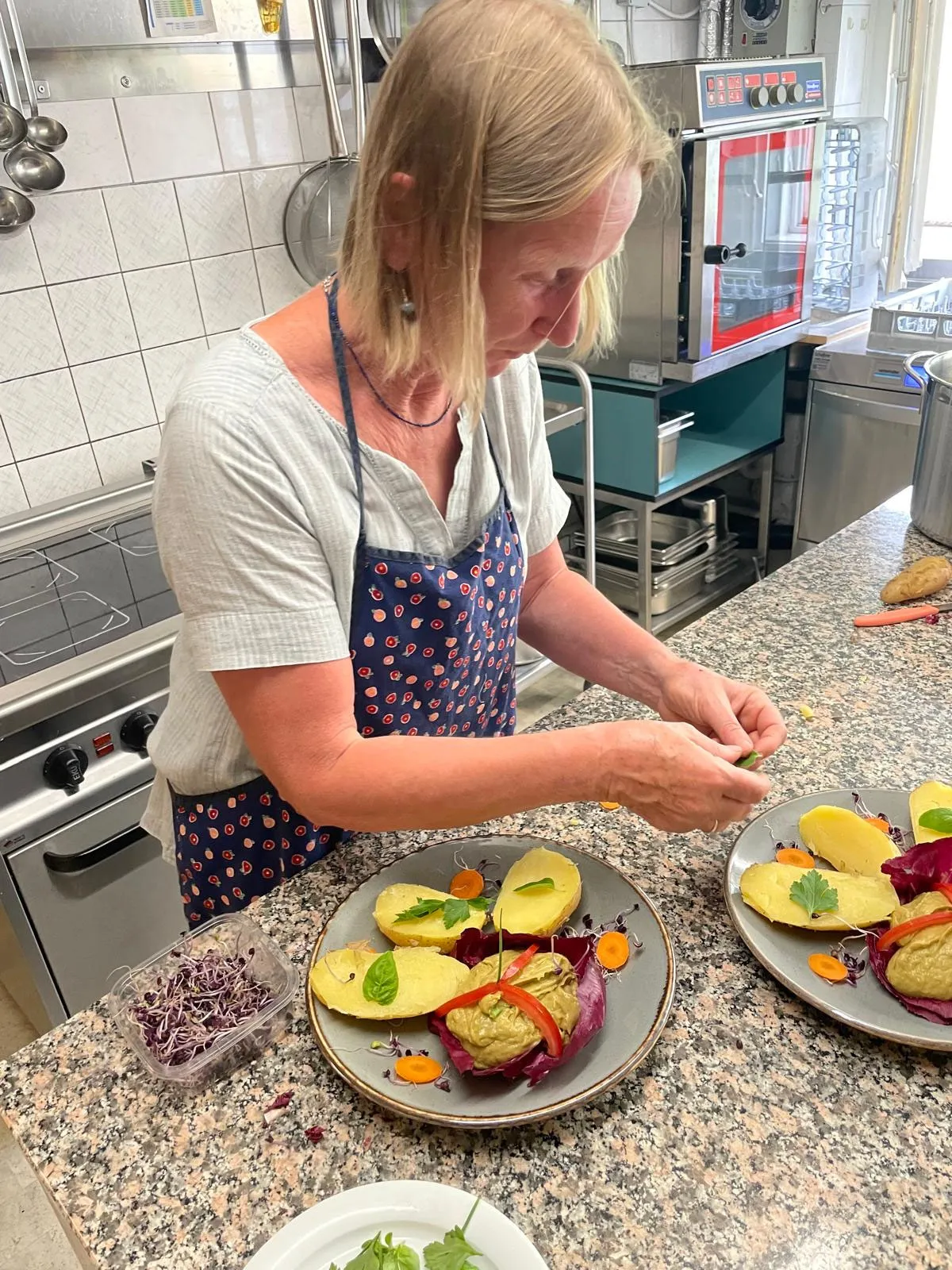 Eine Mitarbeiterin richtet in der Küche Teller mit Avocadohälften, rotem Gemüse und frischen Kräutern an