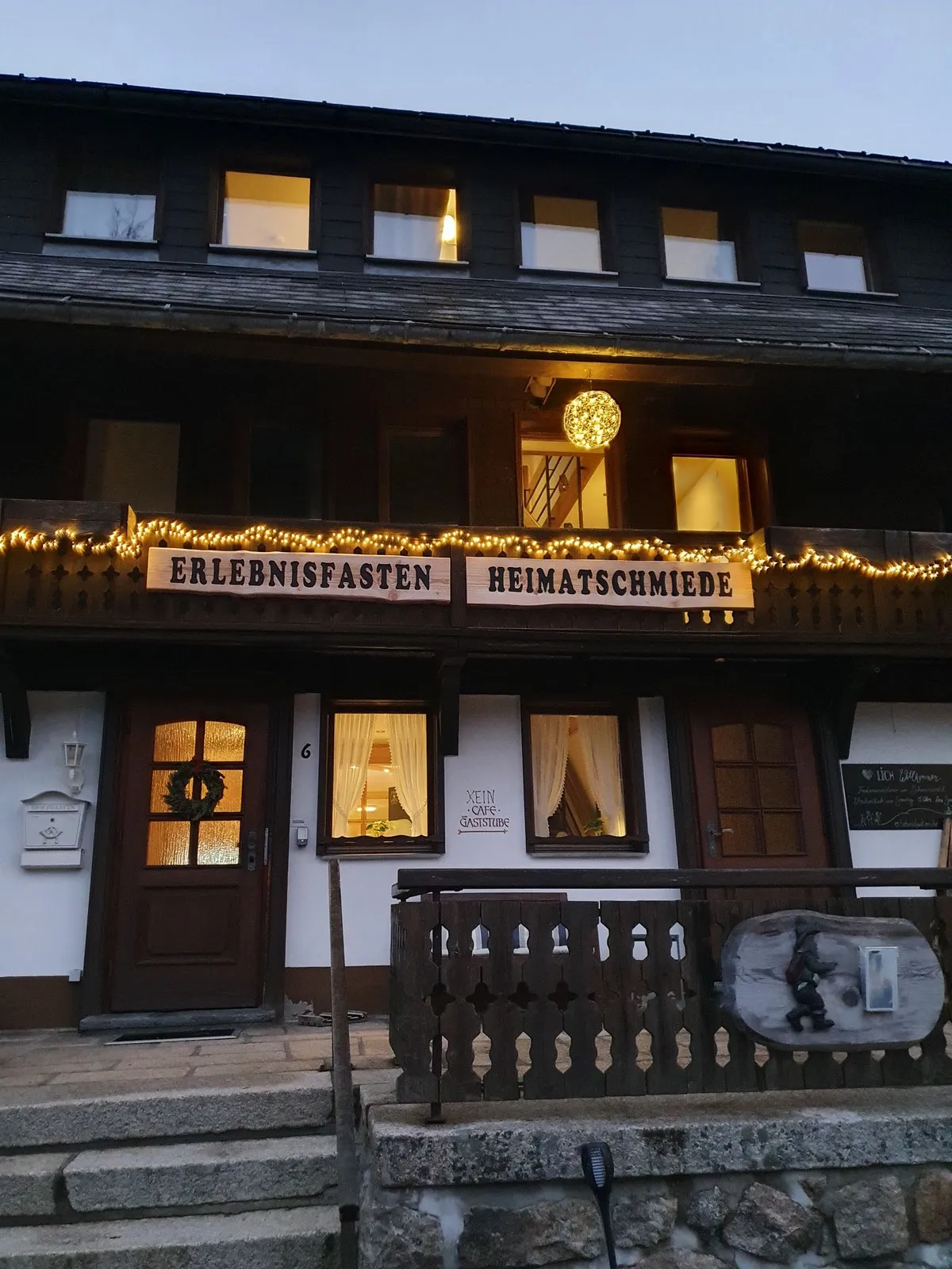 Die Heimatschmiede am Abend: erleuchtete Fenster, Lichterkette und das Schild „Erlebnisfasten Heimatschmiede“ über dem Eingang