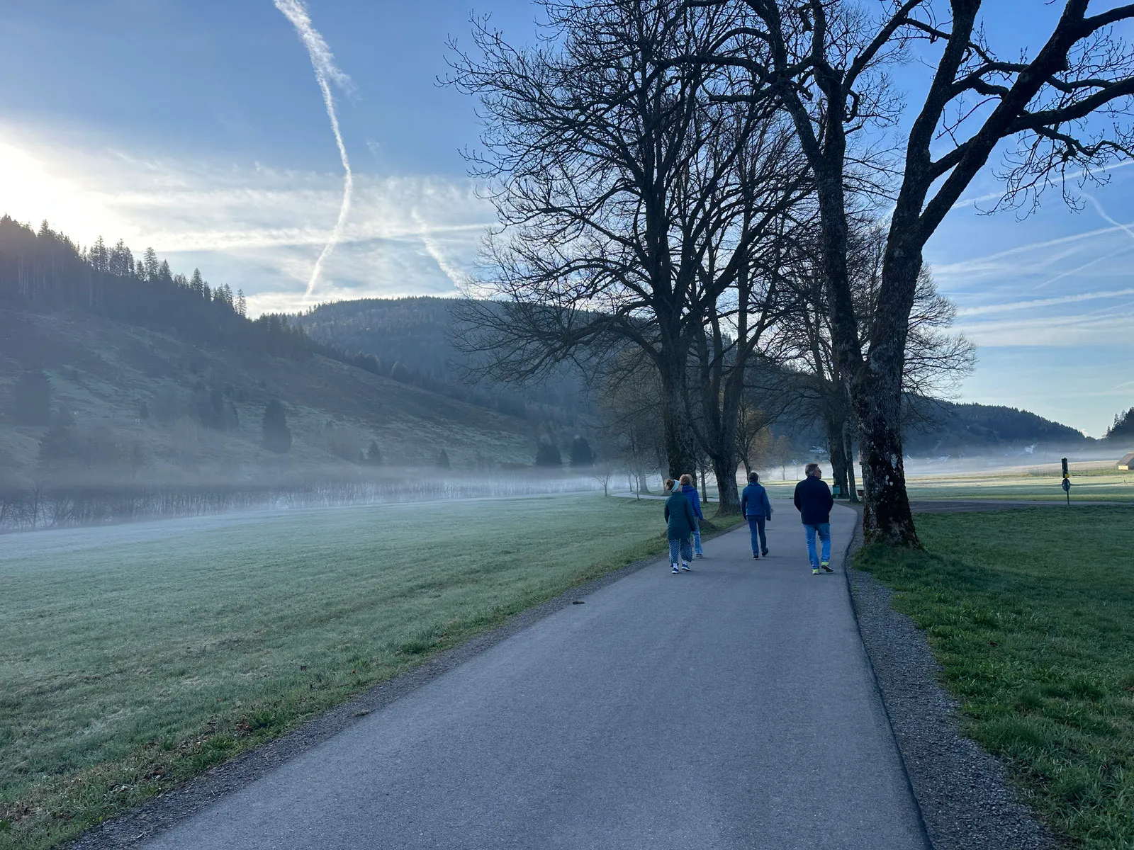 Gäste gehen am frühen Morgen auf einem Weg durch ein Tal, über den Wiesen liegt Nebel