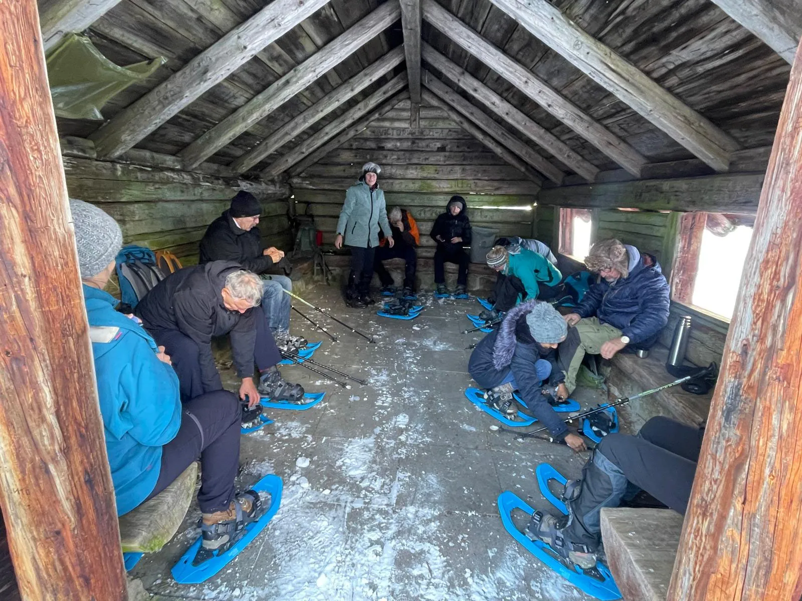 Gäste ziehen in einer Holzhütte ihre Schneeschuhe an