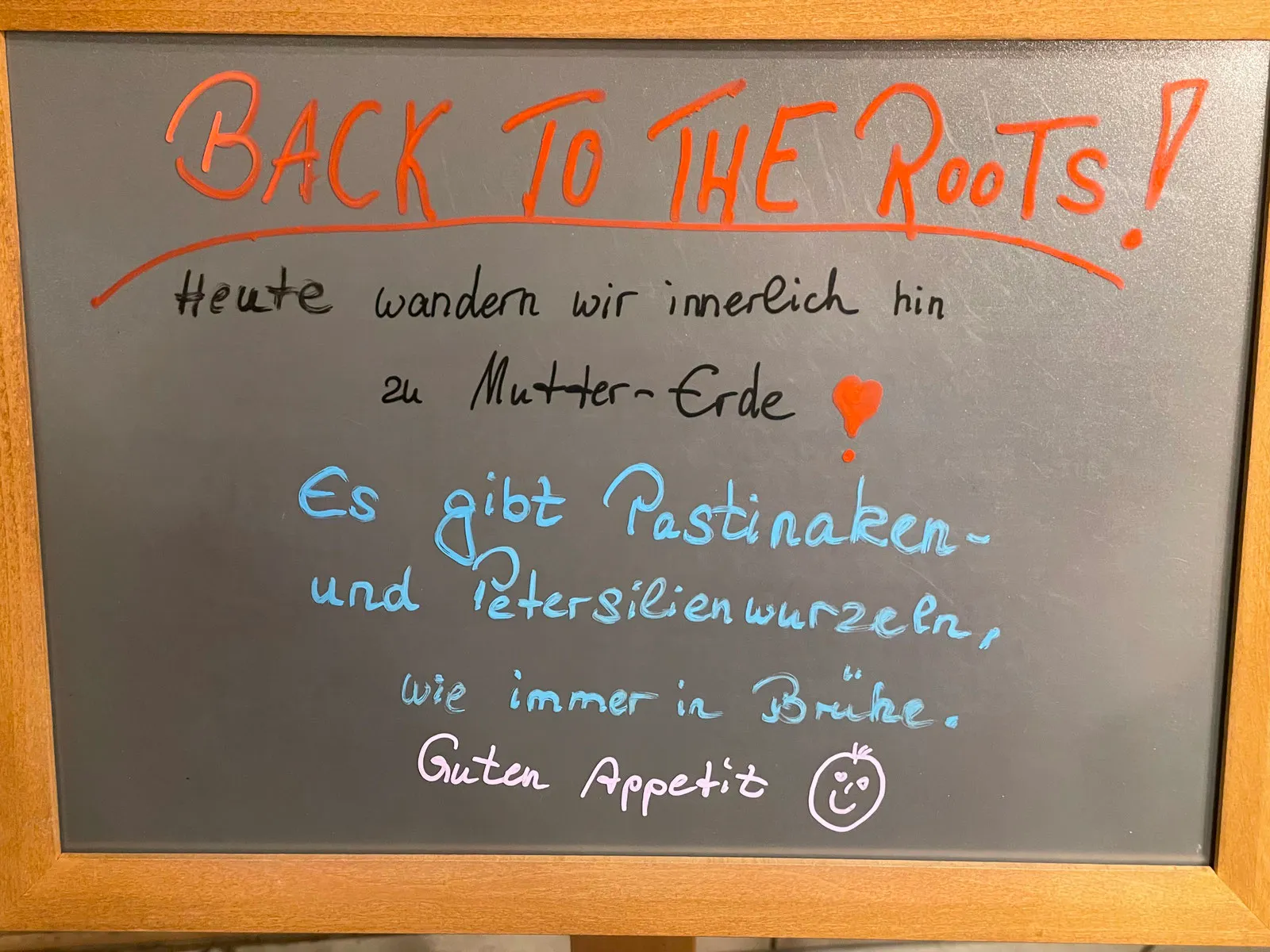 Kreidetafel: „Back to the Roots! Heute wandern wir innerlich hin zu Mutter Erde. Es gibt Pastinaken- und Petersilienwurzeln, wie immer in Brühe. Guten Appetit“
