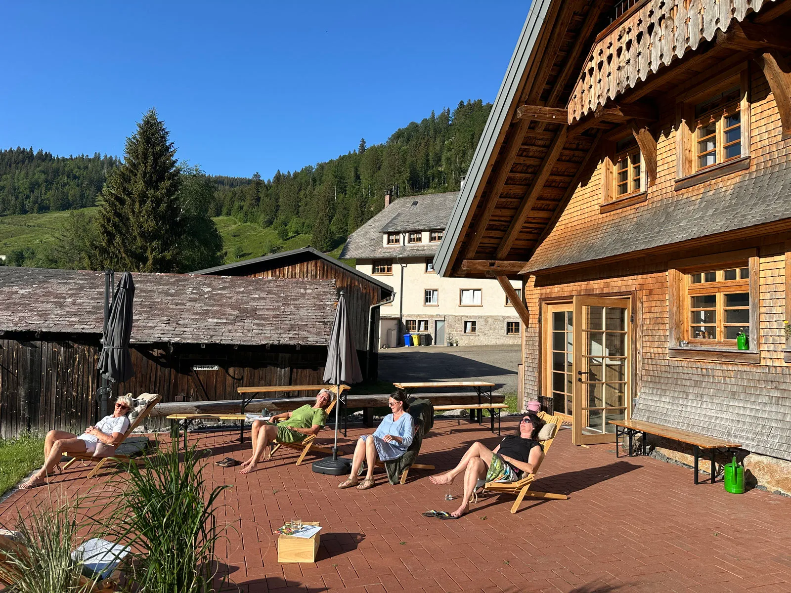 Gäste entspannen in Liegestühlen auf der sonnigen Terrasse vor dem Bruderhof