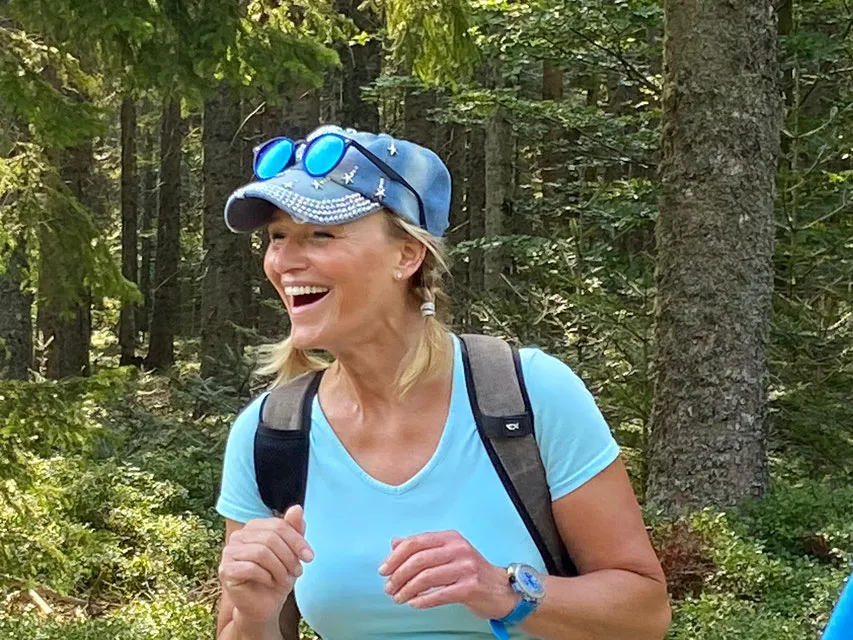 Ute lacht, mit Schirmmütze und Rucksack im Wald